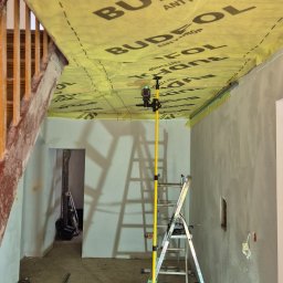 Mariusz Górnicki - Montaż folii paroizolacyjnej Budfol na suficie podwieszanym. Widoczna drabina, poziomica laserowa i fragment schodów. Przygotowanie do dalszych prac wykończeniowych.