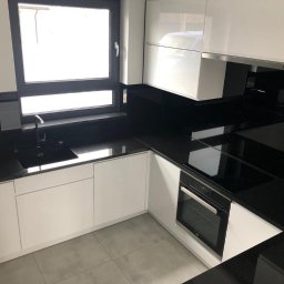 Dawid Szablewski - Nowoczesna kuchnia z czarnym blatem kamiennym i białymi szafkami. Minimalistyczny design, okno nad zlewem, płyta indukcyjna wkomponowana w blat.