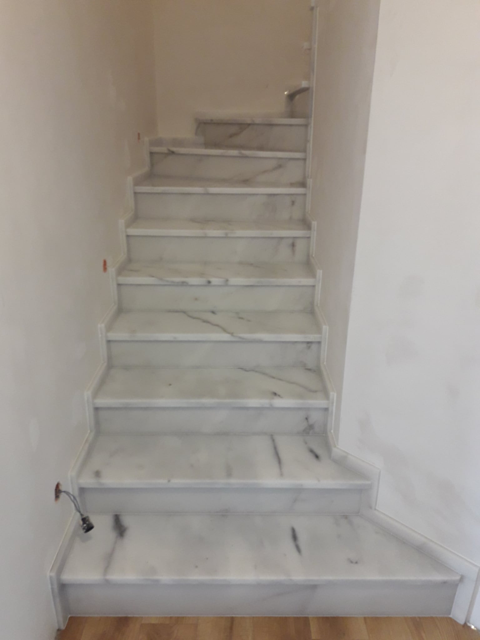 Marmurowe schody wewnętrzne z białego kamienia z szarymi żyłkami, wykonane w Paszowicach. Widok z dołu, jasne wnętrze, minimalistyczny design.