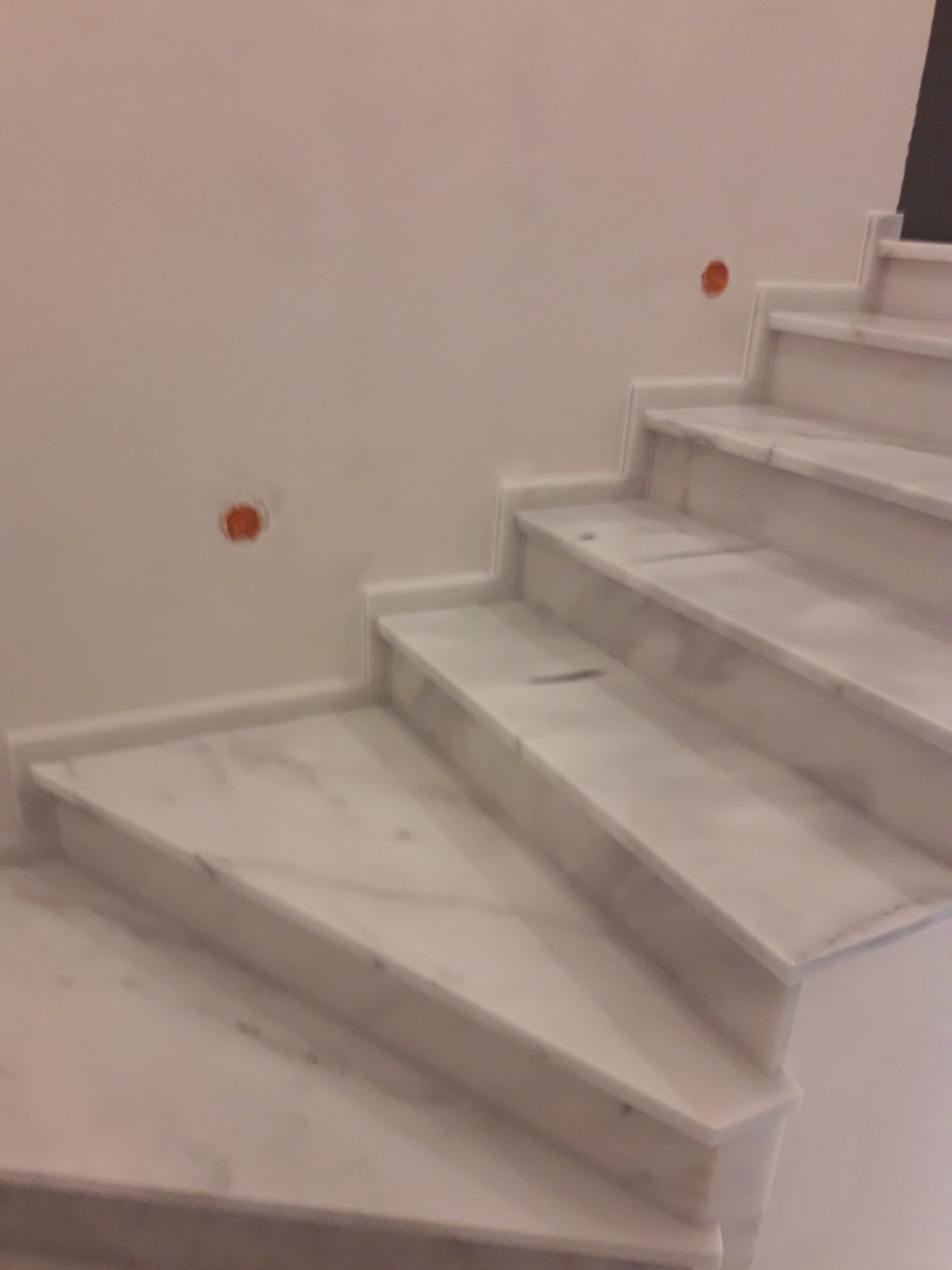 Marmurowe schody wewnętrzne z widocznymi śladami po instalacji elektrycznej na ścianie. Ujęcie z dołu, podkreślające fakturę kamienia i minimalistyczny design.