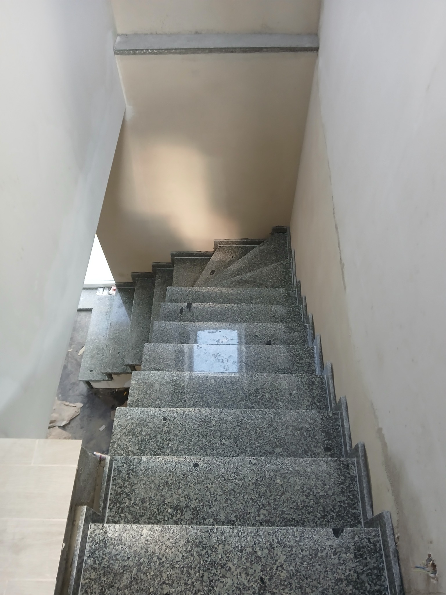 Granitowe schody wewnętrzne w trakcie montażu, widok z góry. Szare stopnie z widoczną fakturą kamienia, surowe ściany w tle. Częściowo widoczne płytki podłogowe.