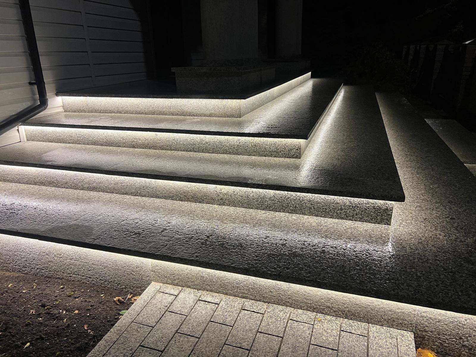 Granitowe schody zewnętrzne z subtelnym oświetleniem LED, podkreślającym strukturę kamienia i nowoczesny design. Nocna sceneria.