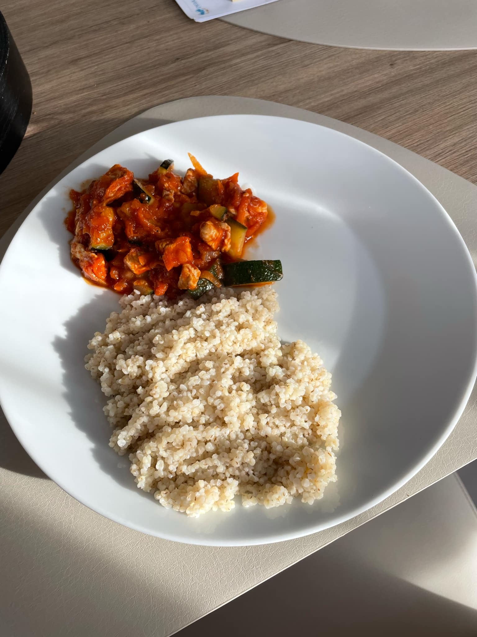 Porcja kaszy bulgur i warzywnego gulaszu na białym talerzu, w naturalnym świetle. Zdjęcie z góry ukazuje gotowy posiłek.