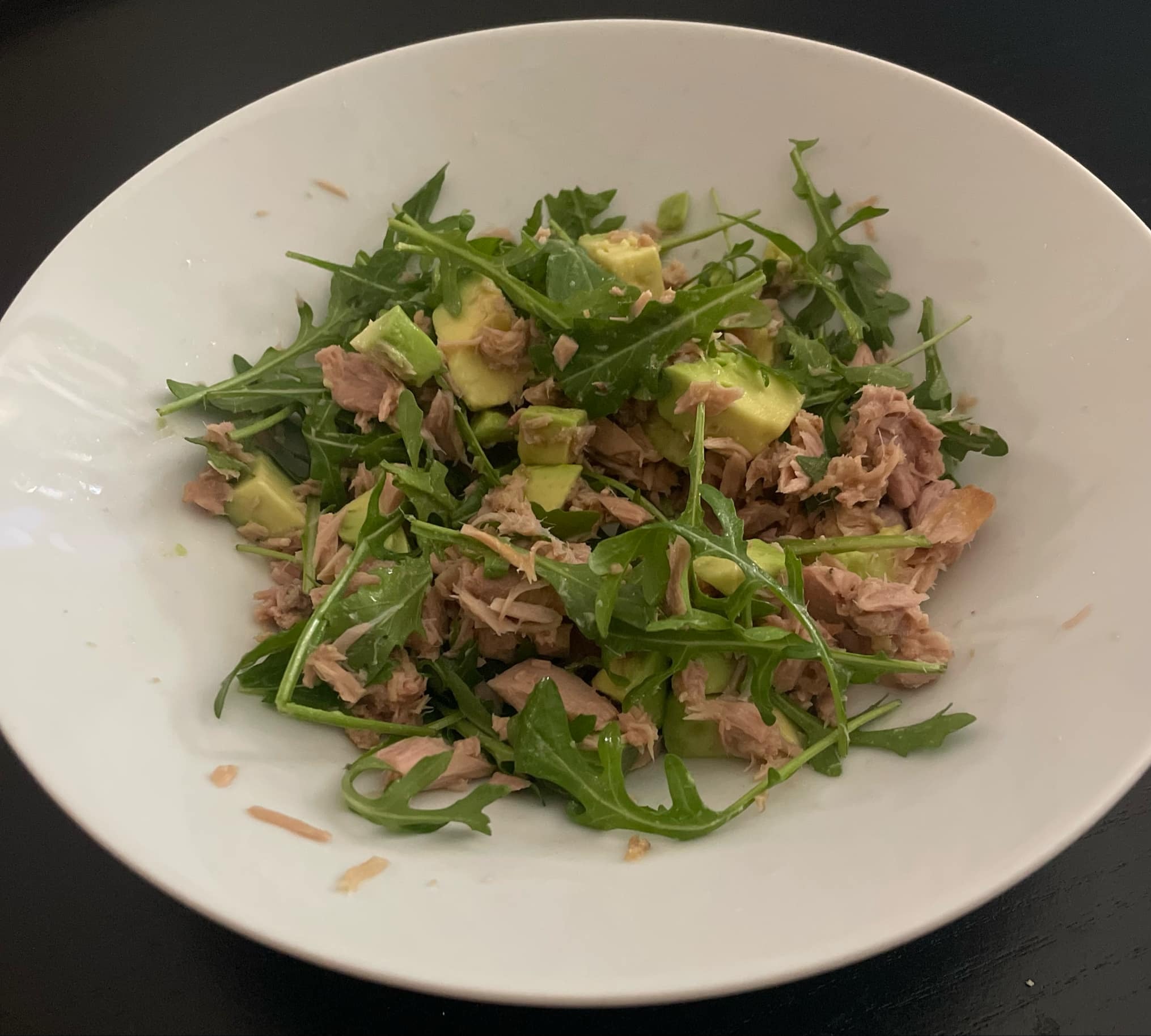 Sałatka z tuńczykiem i awokado na białym talerzu, zielenina na wierzchu, na ciemnym tle. Zdjęcie z bliska, widoczne kawałki tuńczyka i awokado.