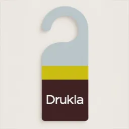 Kolorowy zawieszka na klamkę z napisem 'Drukla', w odcieniach szarości, brązu i ż&oacute;łci, na kremowym tle. Minimalistyczny design.