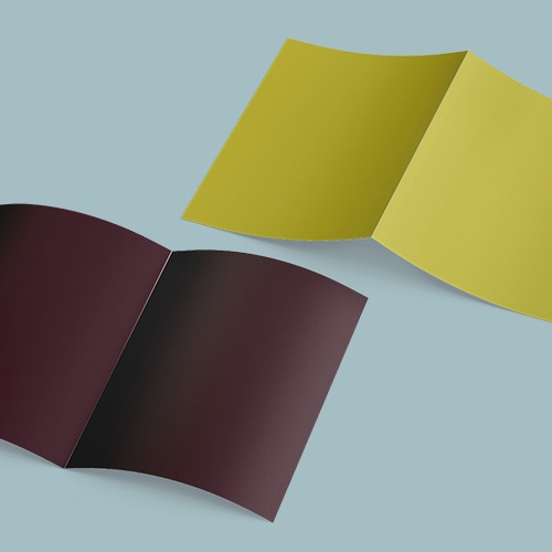 Dwie otwarte broszury: bordowa i oliwkowa, leżące na jasnoniebieskim tle. Broszury bez nadruku, pokazujące formę i kolorystykę.