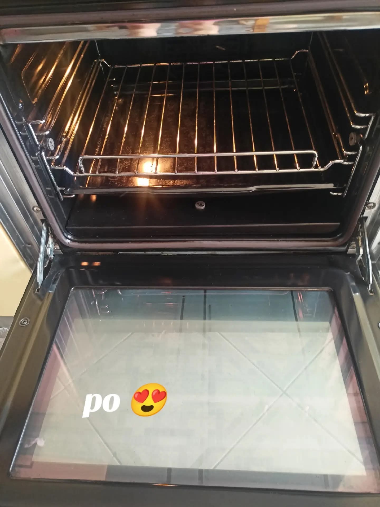 Wnętrze czystego piekarnika po sprzątaniu, widoczne metalowe ruszty i błyszcząca powierzchnia. Na szybie piekarnika napis 'po' z emotikoną z oczami w kształcie serc.