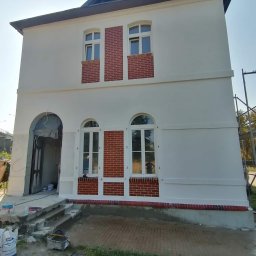 Paweł Tomalski - Dwukondygnacyjny budynek po renowacji elewacji: białe ściany z ceglanymi akcentami wokół okien i u podstawy. Widoczne materiały budowlane i narzędzia.