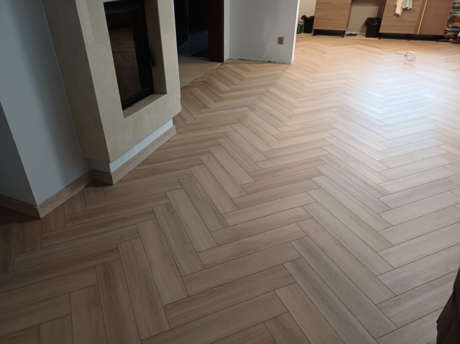 Ułożona podłoga z paneli w jodełkę, widok na kominek i fragment pomieszczenia w Gdańsku. Jasne panele, listwy przypodłogowe.