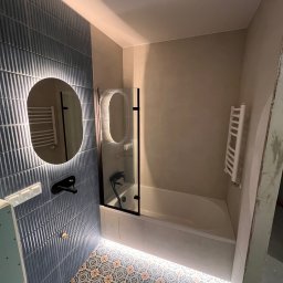 Yauheni Zabarouski - Wykończona łazienka z niebieskimi płytkami, okrągłym lustrem z podświetleniem LED, kabiną prysznicową i wzorzystą podłogą. Grzejnik drabinkowy na ścianie.