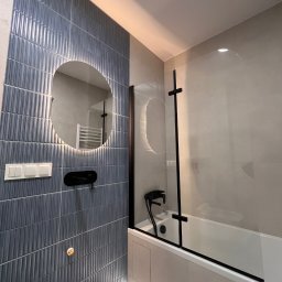 Yauheni Zabarouski - Nowoczesna łazienka z niebieskimi płytkami, okrągłym lustrem z podświetleniem i czarną armaturą. Na podłodze wzorzyste płytki. Kabina prysznicowa ze szklanym panelem.