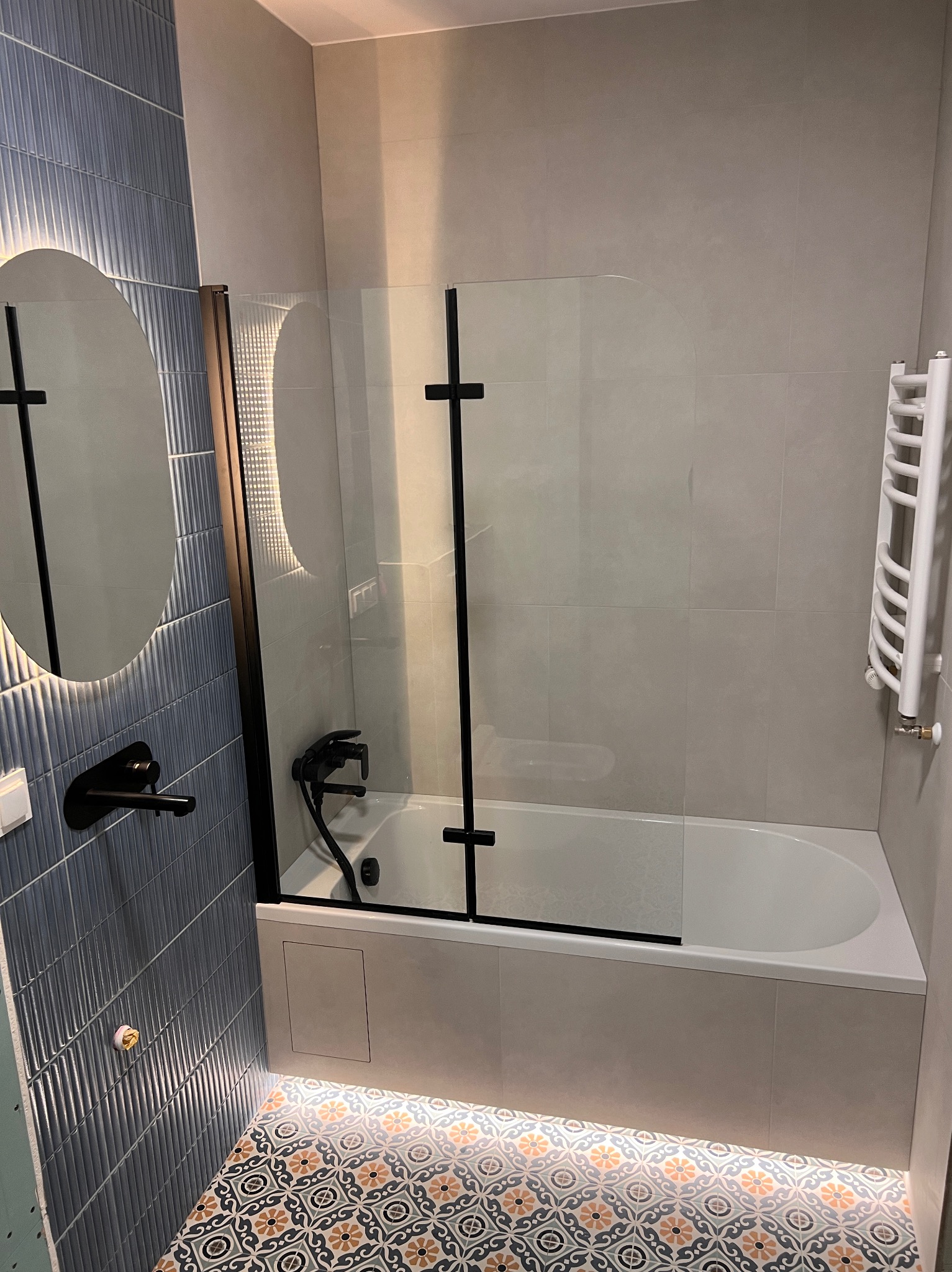 Nowoczesna łazienka z wanną i szklanym parawanem, podświetlaną podłogą w marokańskie wzory, owalnym lustrem z podświetleniem i czarną armaturą.