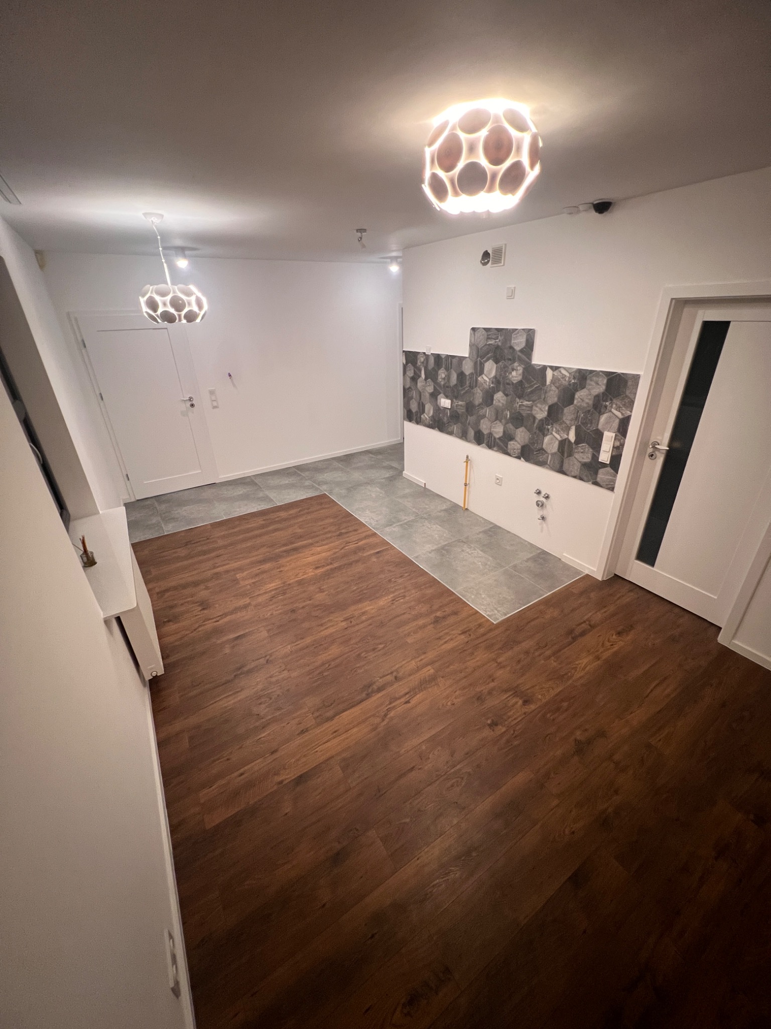 Wykończona podłoga z paneli i fragment ściany z płytkami heksagonalnymi w kuchni we Wrocławiu. Widoczne lampy sufitowe i białe drzwi.