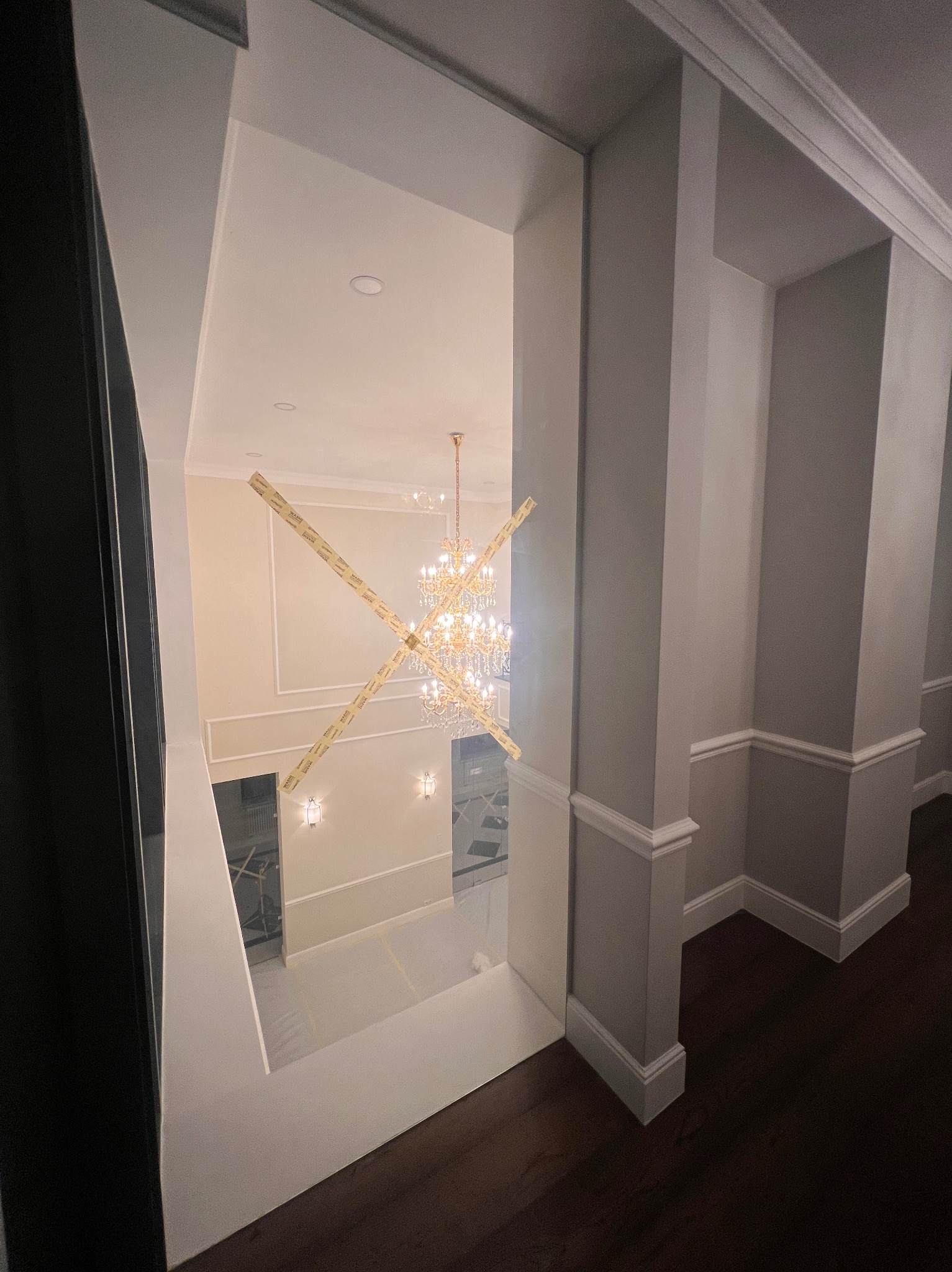 Wysoki hol z dekoracyjnym żyrandolem w trakcie prac wykończeniowych. Widoczne zabezpieczenia na ścianach i podłodze. Ujęcie z góry, z perspektywy schodów.