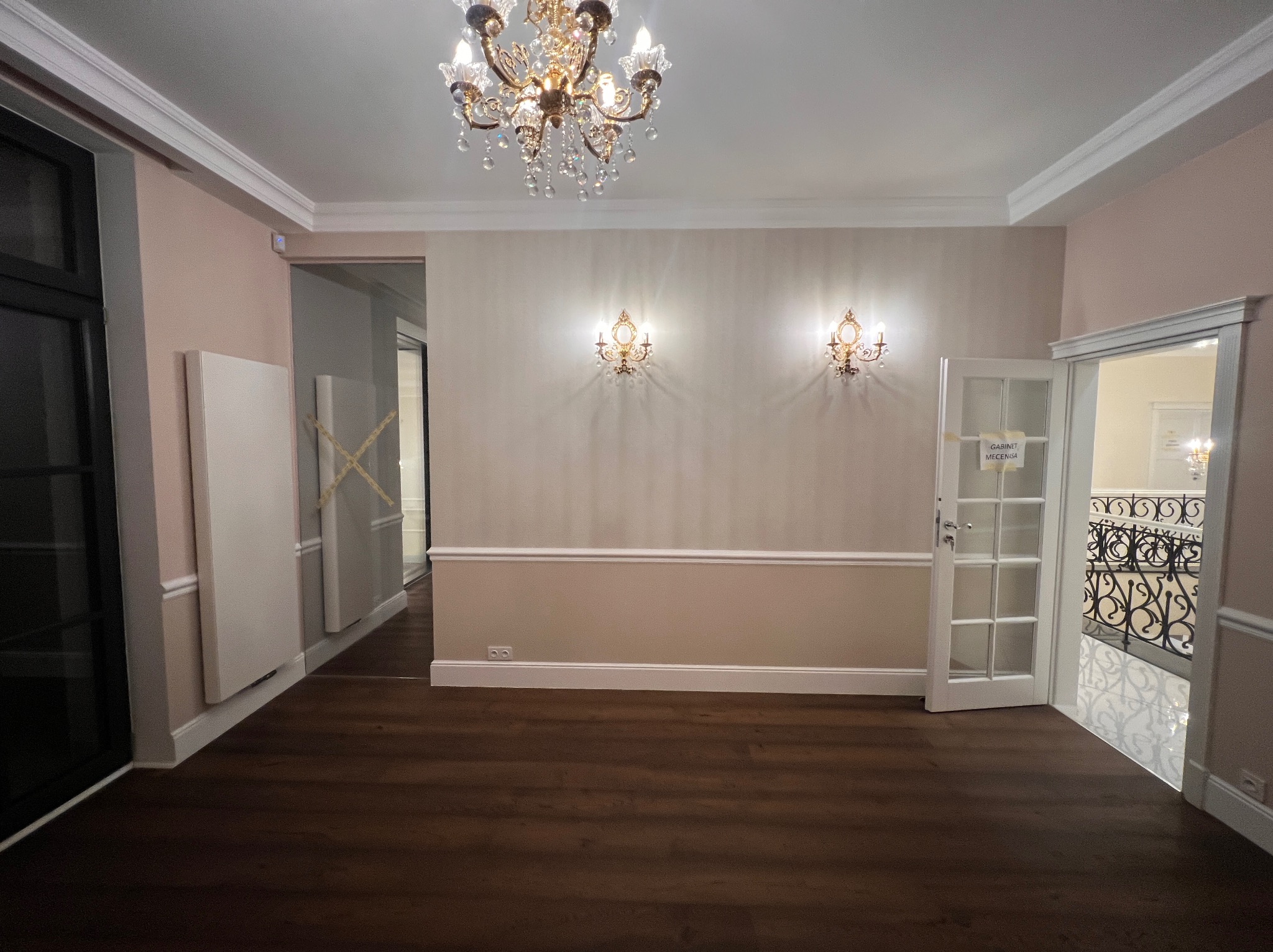 Eleganckie wnętrze po remoncie: parkiet, listwy przypodłogowe, dekoracyjne kinkiety, żyrandol kryształowy, drzwi z szybkami. Widok na klatkę schodową.
