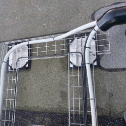 Ampivolt Instalacje Elektryczne - Klatka montażowa z przewodami elektrycznymi na dachu, widok z góry. Białe rury i czarne przewody przymocowane do metalowej konstrukcji. Fragment buta w prawym dolnym rogu.