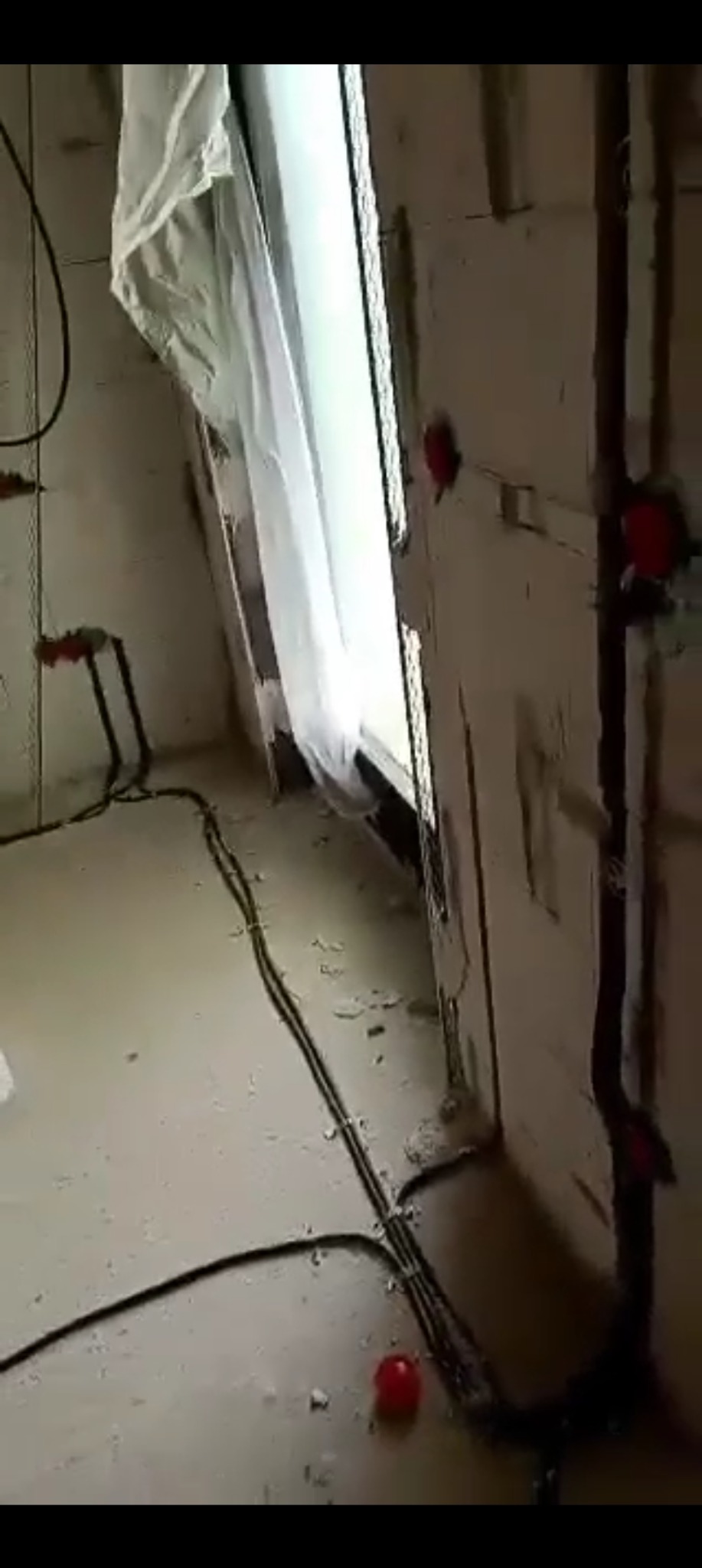 Wnętrze w trakcie remontu: widoczne kable elektryczne, puszki instalacyjne na ścianie z surową, białą cegłą. Okno zabezpieczone folią malarską.