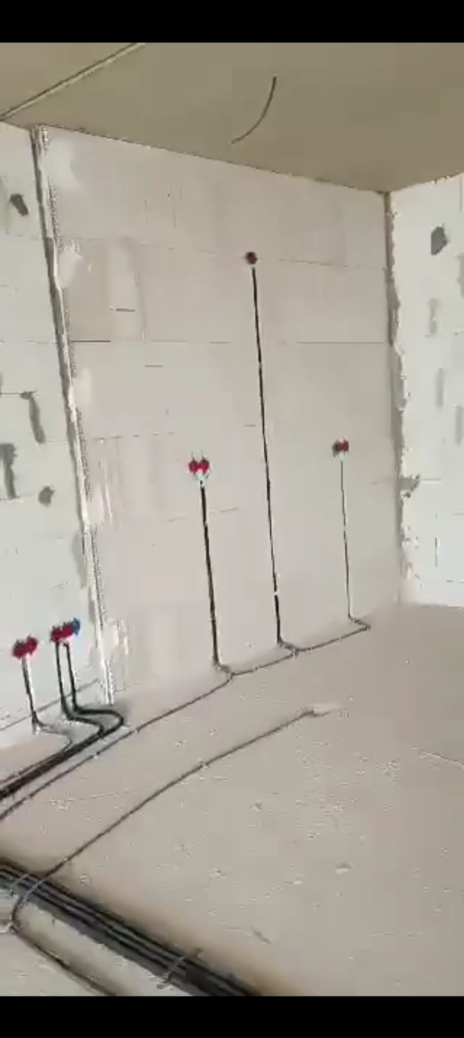 Wnętrze w trakcie prac instalacyjnych: widoczne czarne kable elektryczne prowadzone po ścianach i podłodze, przygotowane do montażu gniazdek i włączników.