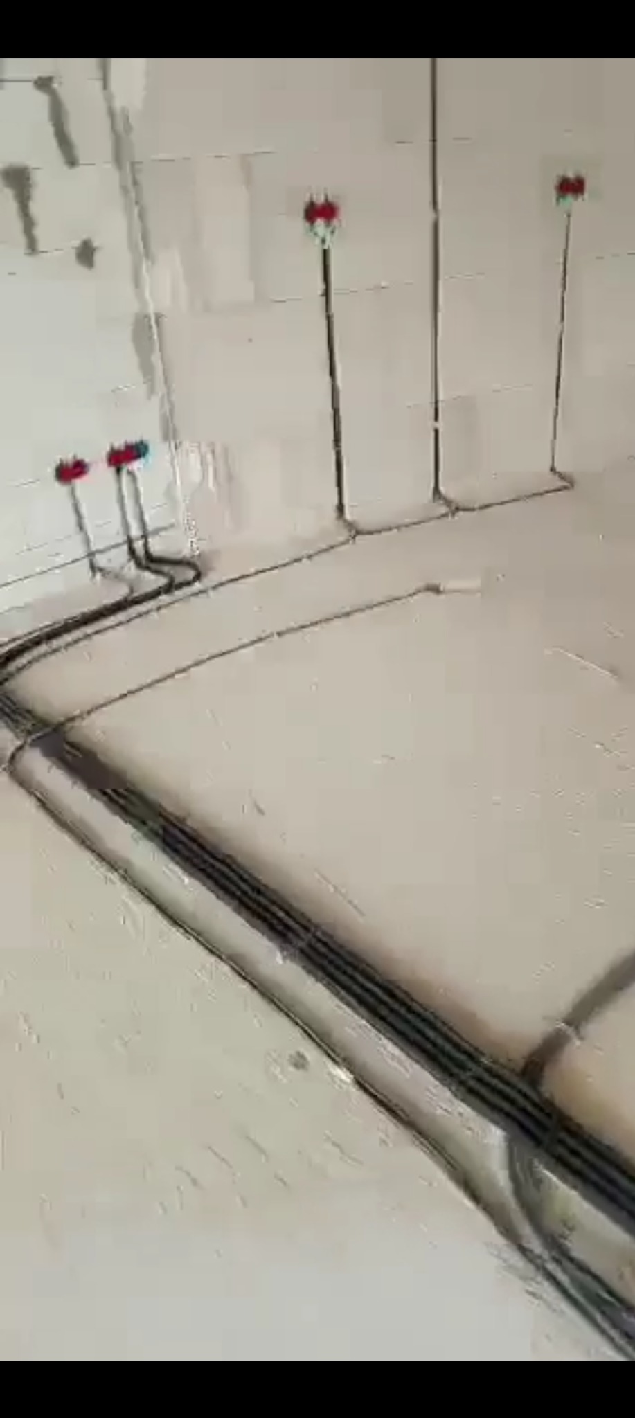Surowy stan instalacji elektrycznej w bruzdach ściany z betonu komórkowego przed tynkowaniem. Widoczne kable i puszki instalacyjne.