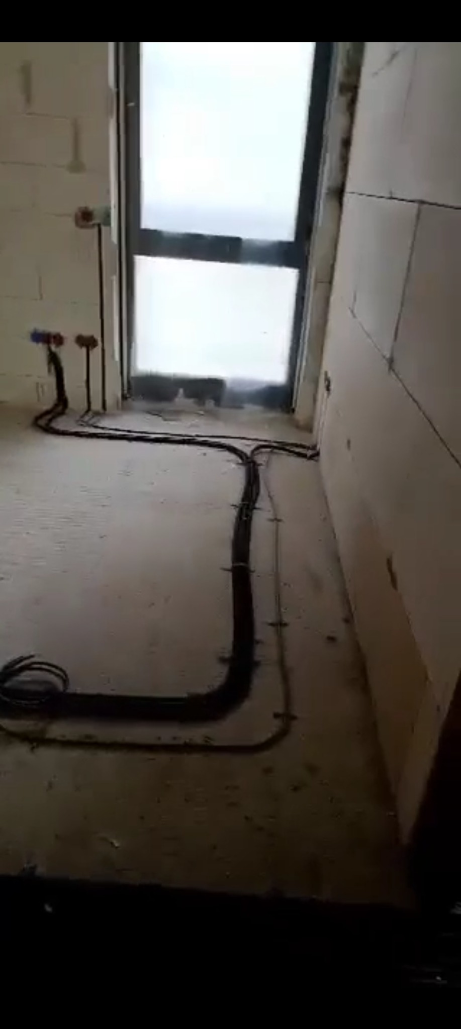 Wnętrze w surowym stanie z rozprowadzoną instalacją elektryczną w peszlach, widoczne puszki instalacyjne. Przewody przymocowane do ściany, okno w tle.