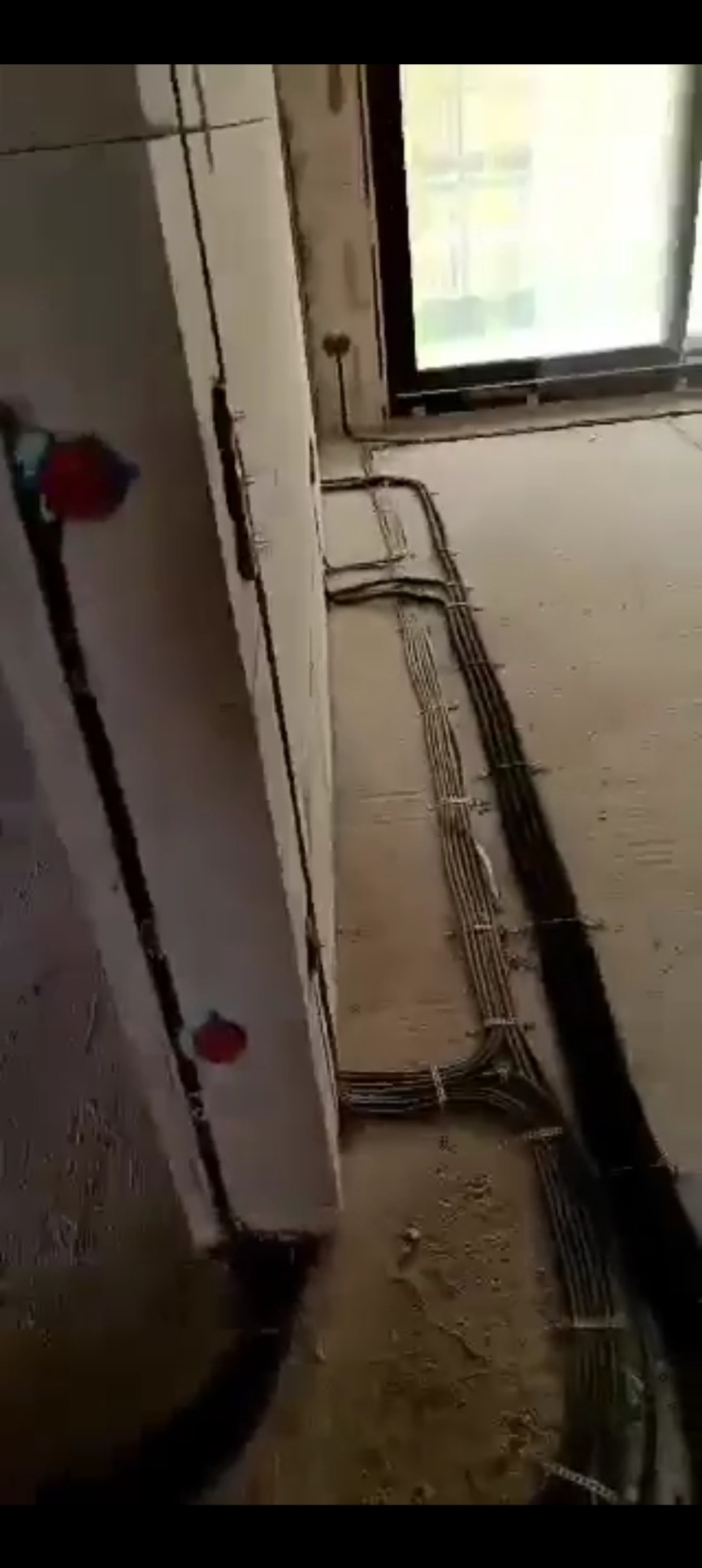 Wnętrze w trakcie remontu: widoczne kable elektryczne ułożone wzdłuż ściany i podłogi, puszki elektryczne na ścianie, okno w tle. Instalacja elektryczna w nowym budynku.