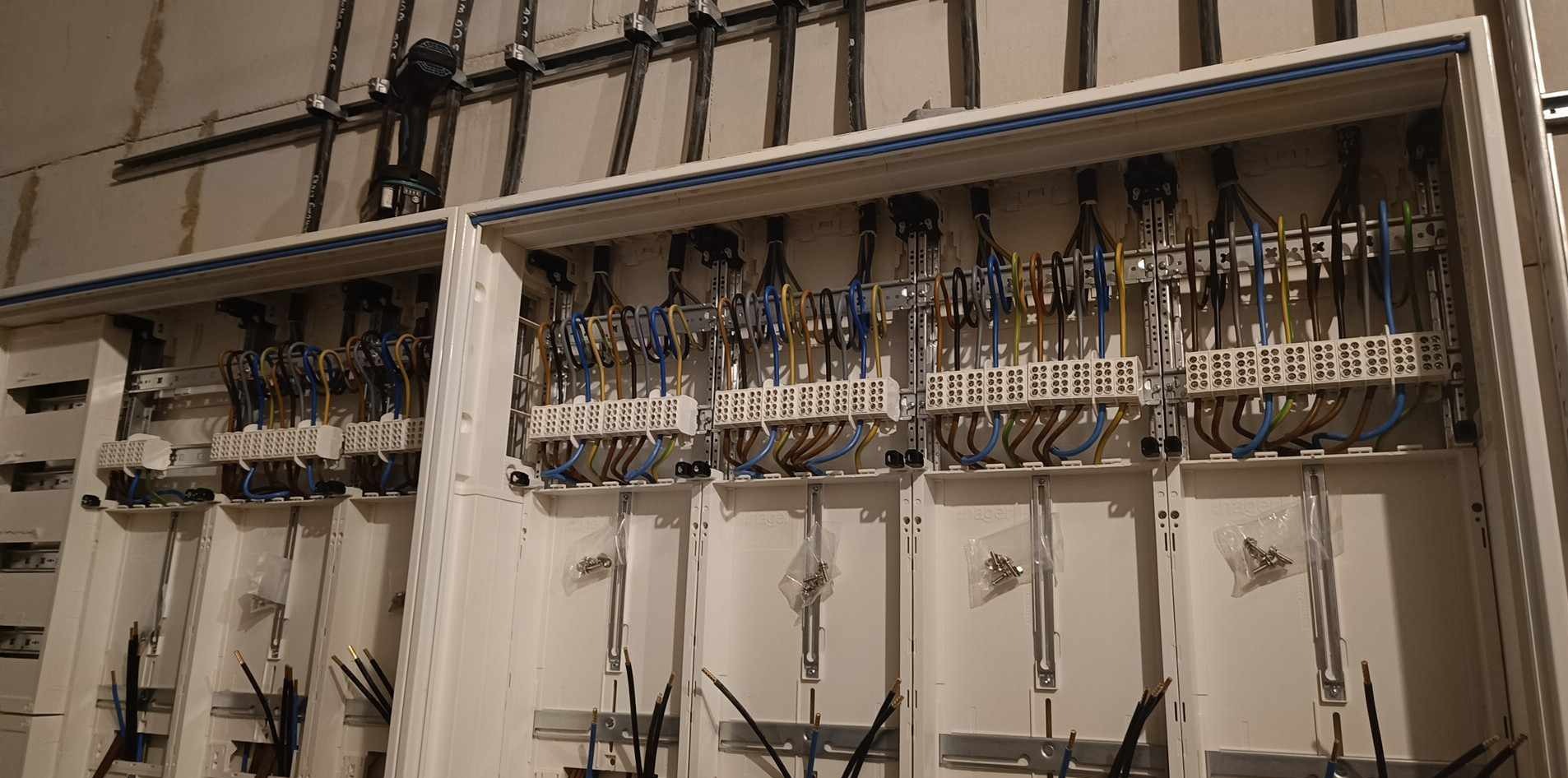 Rozdzielnia elektryczna w trakcie montażu, widoczne kable w różnych kolorach, listwy montażowe i elementy mocujące. Instalacja w stanie surowym.