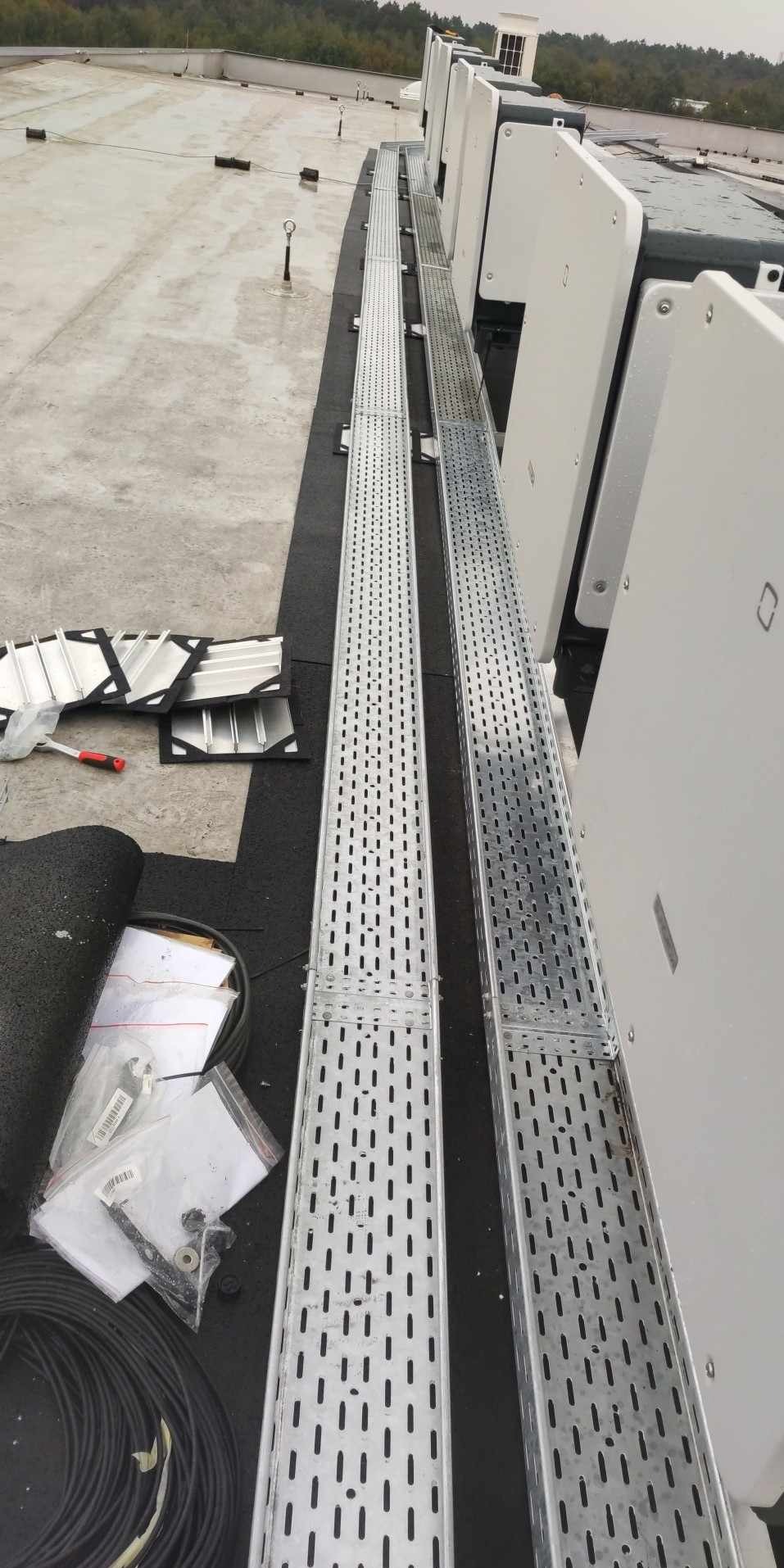 Montaż korytek kablowych na dachu z widocznymi elementami instalacji elektrycznej i narzędziami. Etap prac instalacyjnych.
