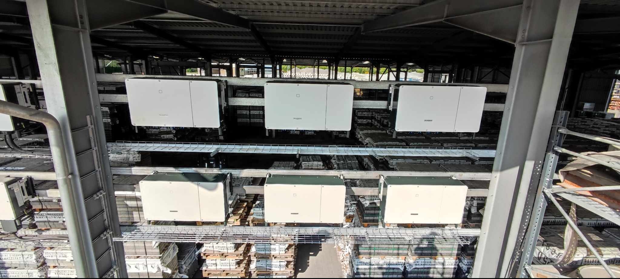 Rozbudowana instalacja fotowoltaiczna z białymi falownikami na regałach w hali przemysłowej, widok z góry, symetryczny układ i metalowa konstrukcja wsporcza.