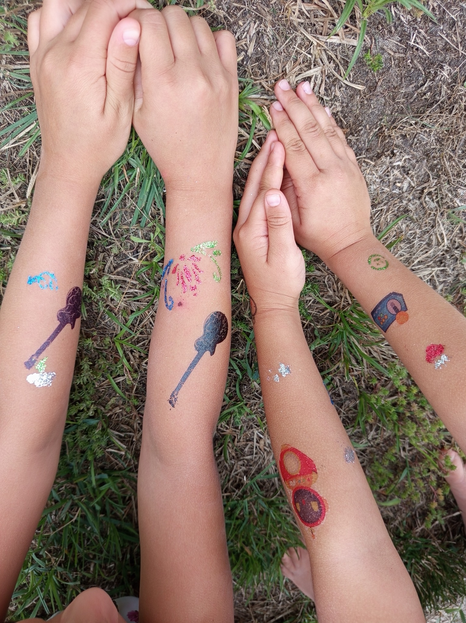 Dziecięce ramiona z brokatowymi tatuażami (gitara, grzyb, konsola) na trawie w Opole Lubelskie. Atrakcja dla dzieci podczas imprezy.