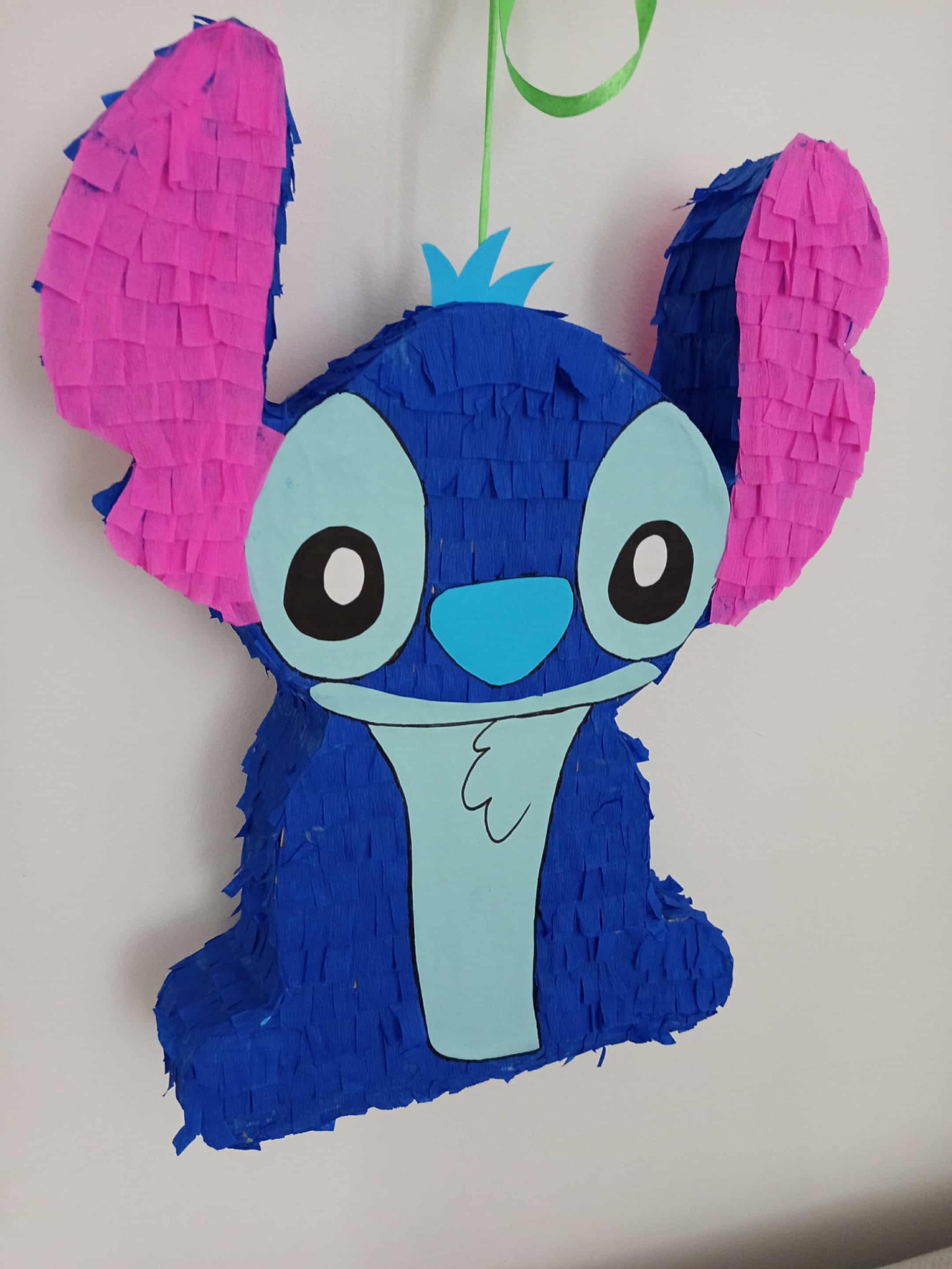 Ręcznie robiona pinata Stitch z niebieskiej i różowej krepy, zawieszona na zielonej wstążce, idealna na urodziny dziecka.