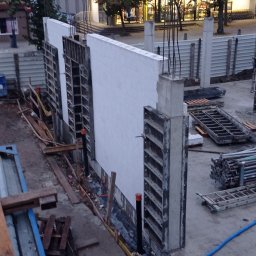 Pitbul AMKD Oleksandr Pitel - Budowa ściany z bloczków betonowych z szalunkiem i wystającymi prętami zbrojeniowymi. Widoczne elementy konstrukcyjne i narzędzia budowlane na placu budowy.