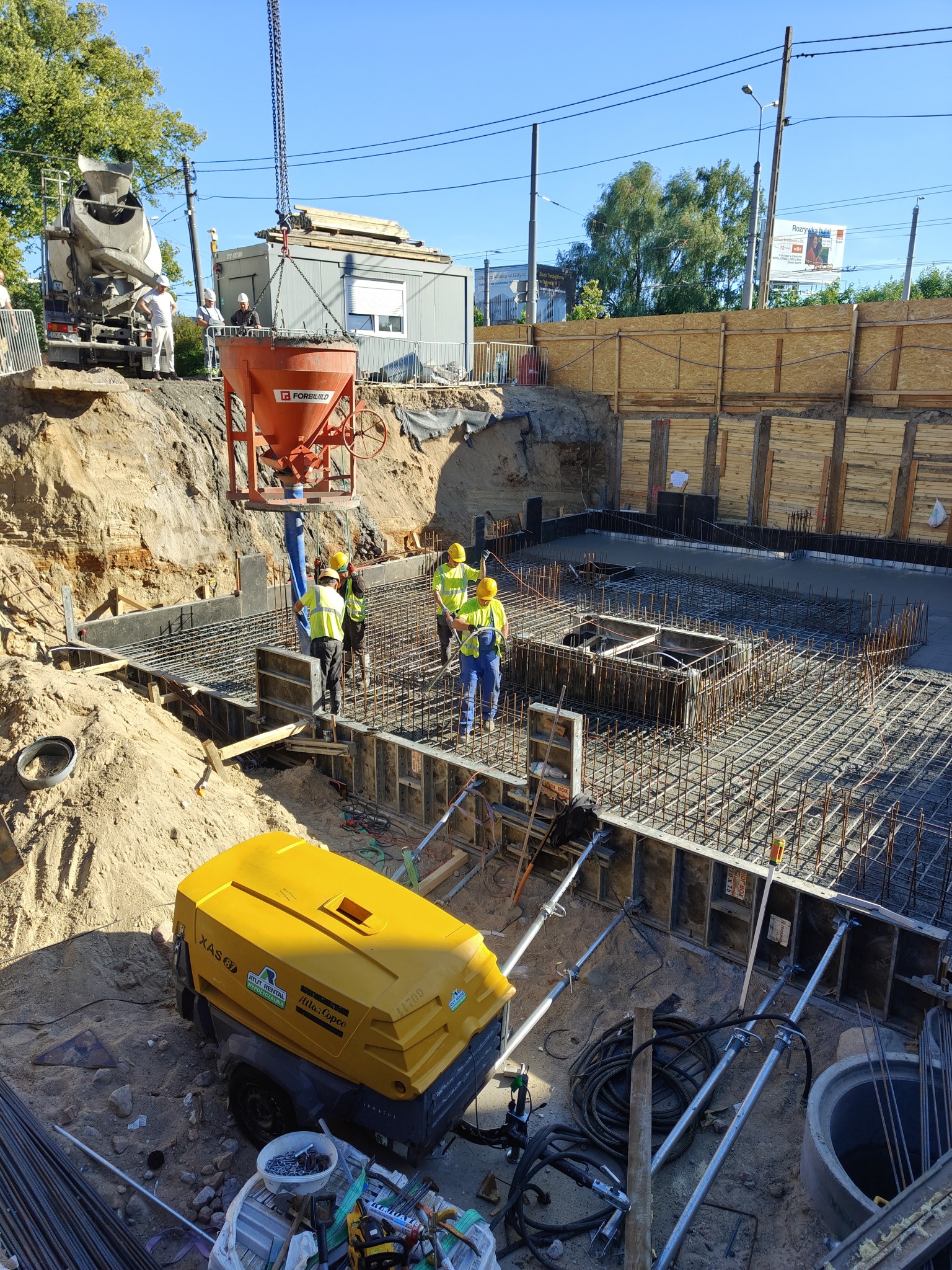 Wylewanie betonu na zbrojenie fundamentów w Rumi. Na budowie widoczni pracownicy w kaskach i żółtych kamizelkach. Na pierwszym planie sprężarka.