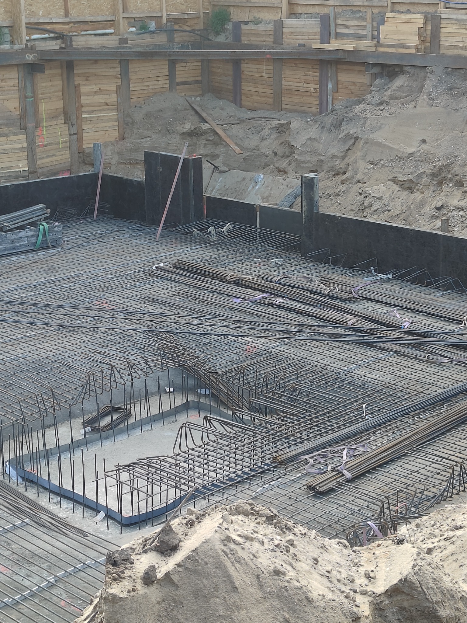 Zbrojenie fundamentu, widoczne pręty stalowe ułożone w siatkę, przygotowane do zalania betonem. W tle drewniane szalunki i ziemia.