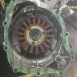 Stojan alternatora motocyklowego z cewkami miedzianymi wewnątrz obudowy z uszczelką, widoczne ślady oleju, naprawa motocykla.