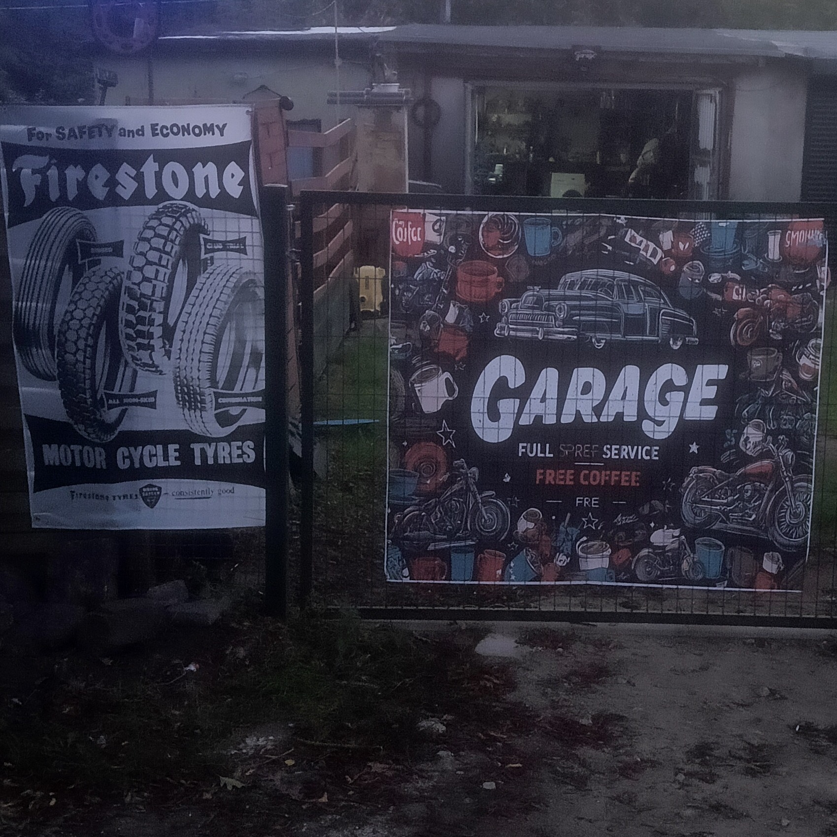 Dwa banery reklamowe: Firestone - opony motocyklowe i Garage - pełny serwis, darmowa kawa. Ekspozycja przed warsztatem samochodowym. Niska jakość zdjęcia.