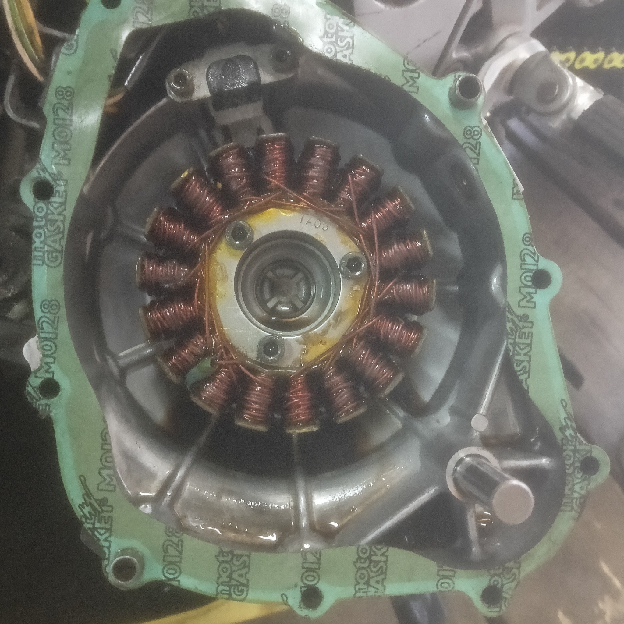 Stojan alternatora motocyklowego z cewkami miedzianymi wewnątrz obudowy z uszczelką, widoczne ślady oleju, naprawa motocykla.