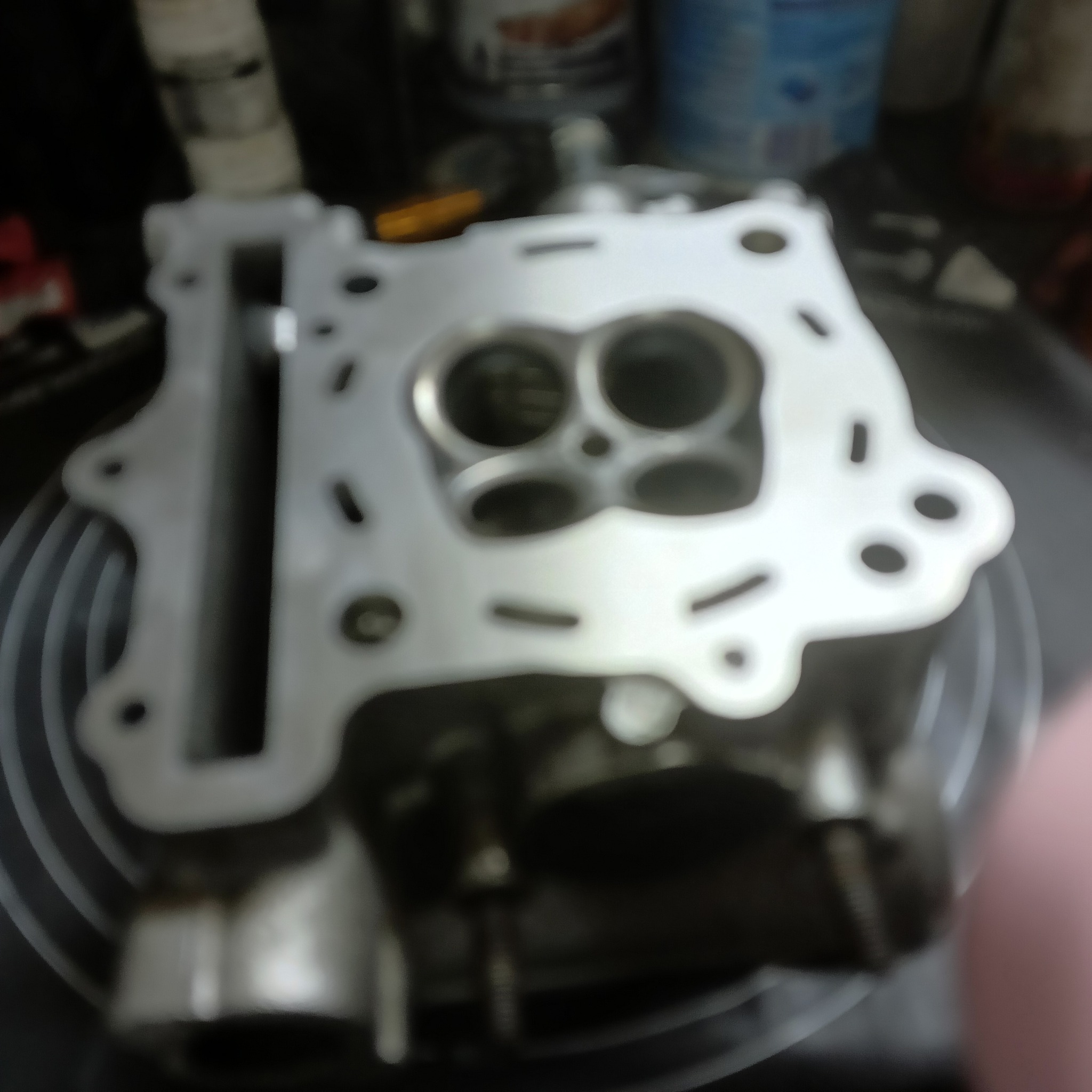 Głowica silnika spalinowego, widoczne zawory i kanały. Element po obróbce, prawdopodobnie czyszczeniu lub planowaniu. Detal w zbliżeniu, na warsztatowym stole.