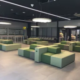 Nowoczesne, modułowe sofy tapicerowane w odcieniach zieleni i szarości w przestrzeni publicznej w Nowej Rudzie. Geometryczny design, minimalistyczne oświetlenie.