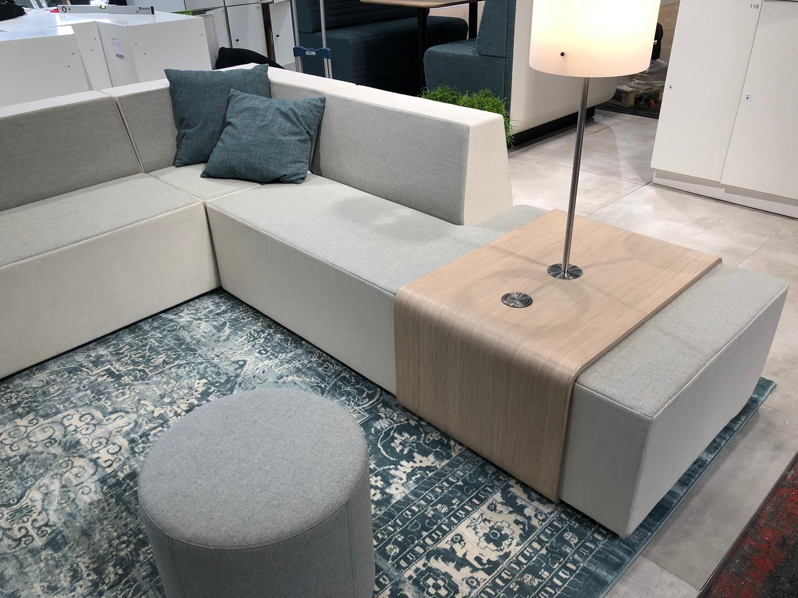 Modułowa sofa z turkusowymi poduszkami i pufą na wzorzystym dywanie, oświetlona lampą. Minimalistyczny design z elementami drewna, tworzący nowoczesną strefę relaksu.