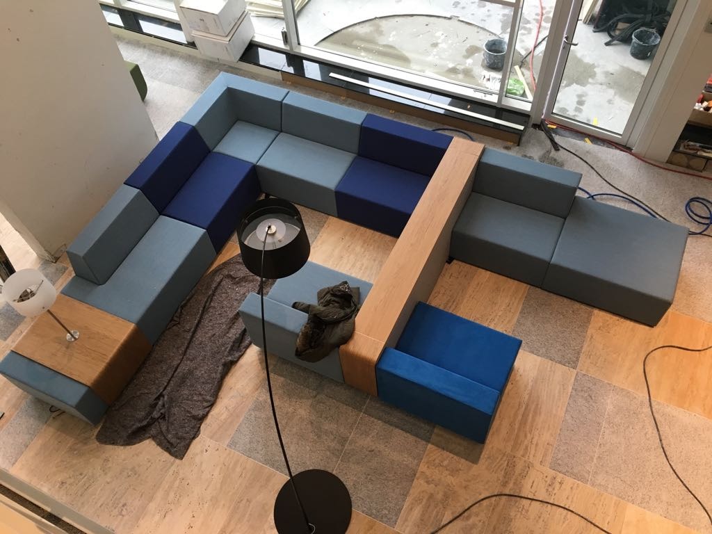 Narożnik modułowy z tapicerką w odcieniach niebieskiego, z drewnianymi elementami, widziany z góry, oświetlony lampami stojącymi, na tle płytek podłogowych.