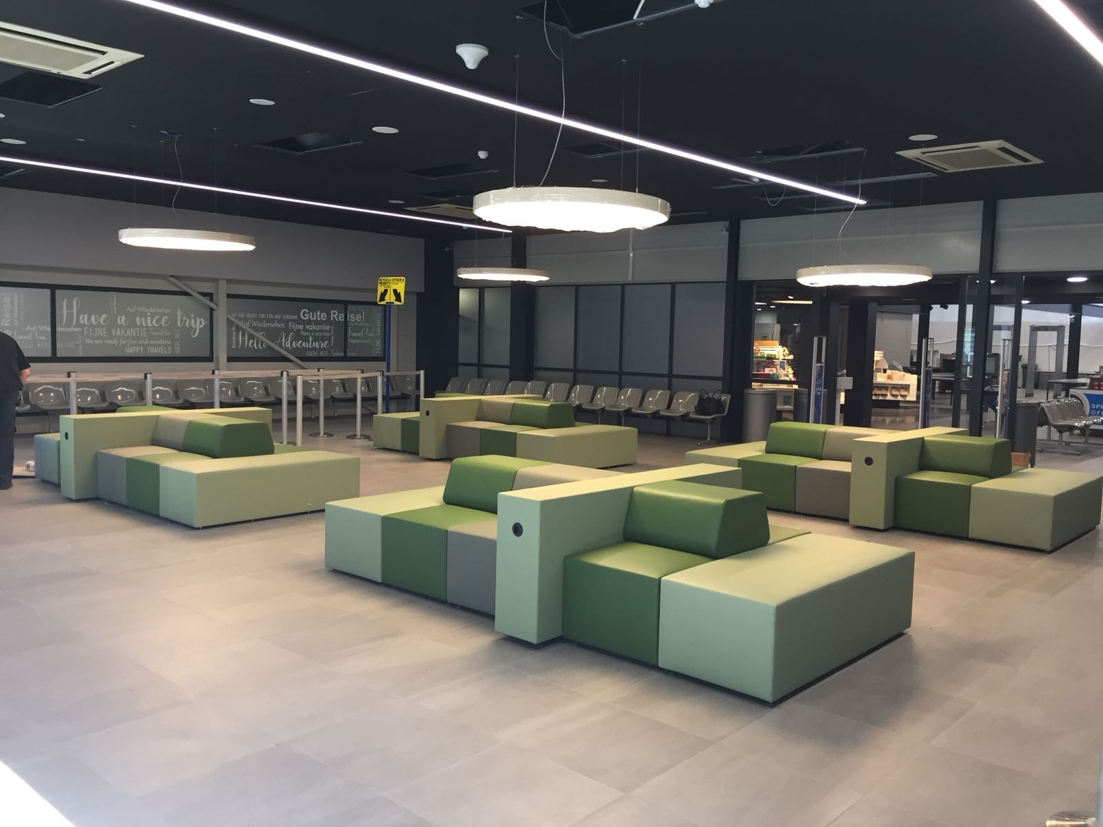 Nowoczesne, modułowe sofy tapicerowane w odcieniach zieleni i szarości w przestrzeni publicznej w Nowej Rudzie. Geometryczny design, minimalistyczne oświetlenie.