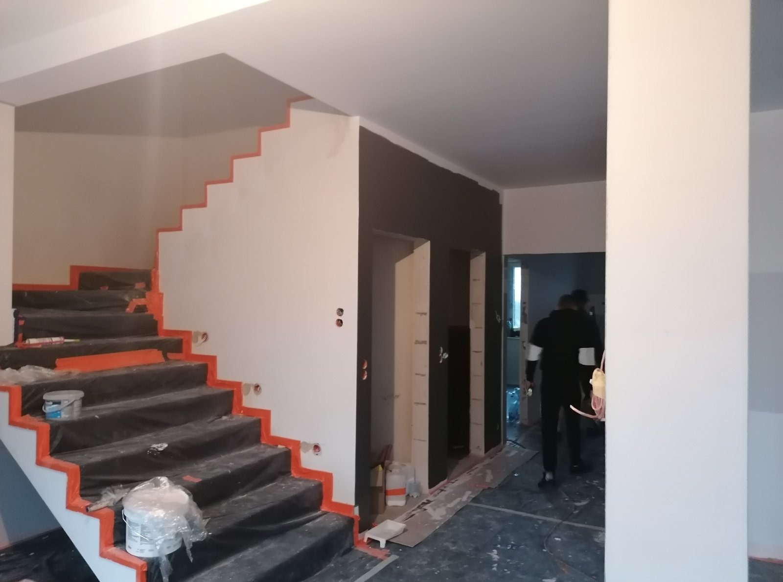 Wnętrze w trakcie prac wykończeniowych: zabezpieczone schody z pomalowanymi na biało ścianami. Widoczne przygotowania do montażu konstrukcji wnękowych.