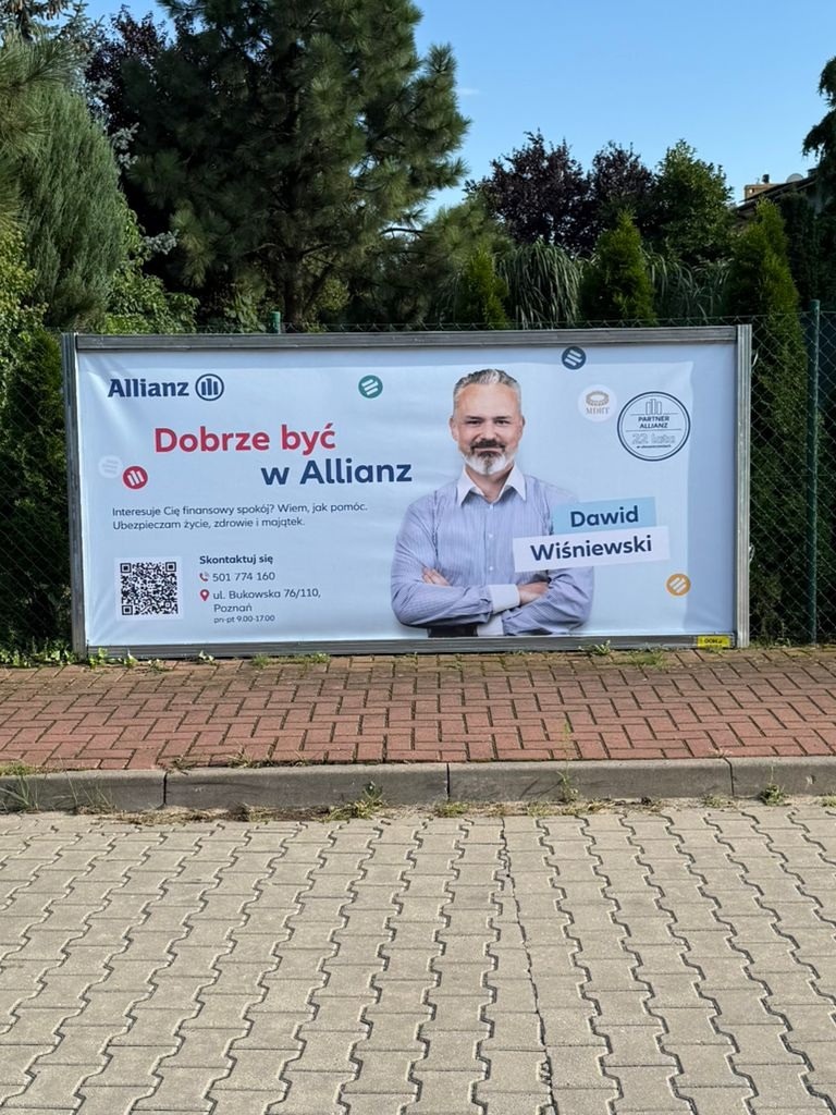 Billboard Allianz z wizerunkiem agenta Dawida Wiśniewskiego. Reklama ubezpieczeń na życie, zdrowie i majątek. Widoczny numer telefonu i adres biura w Poznaniu.