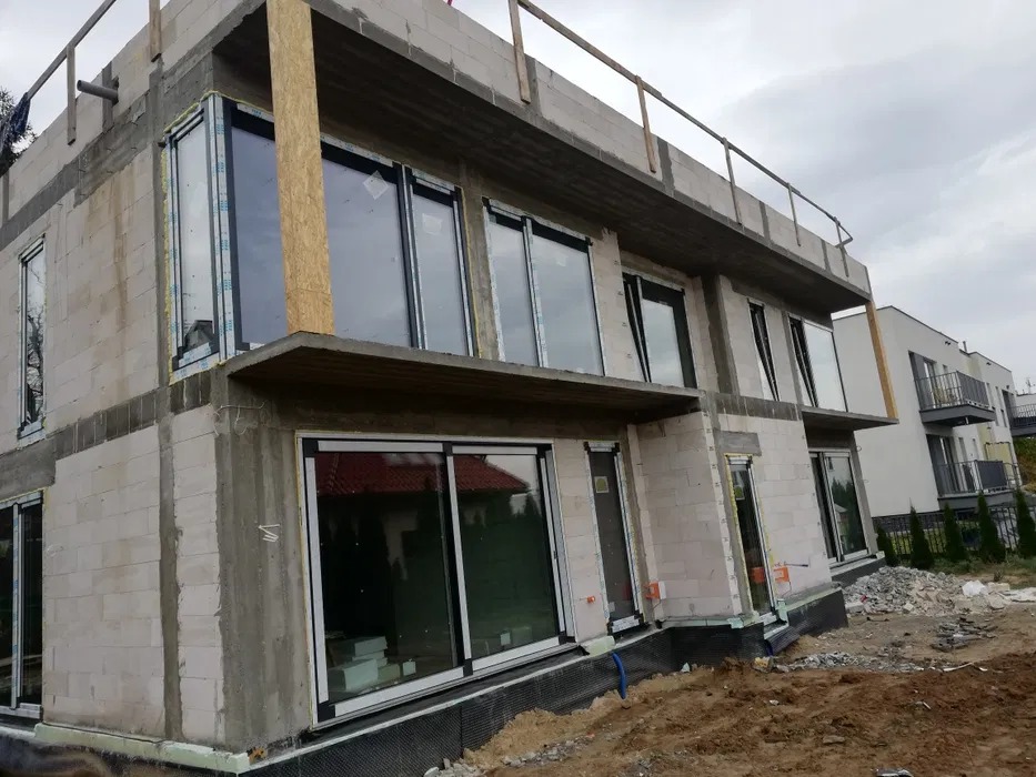 Dwukondygnacyjny budynek z betonu komórkowego w Miłkowie, z dużymi oknami i balkonami, w trakcie budowy, z widocznym zbrojeniem i deskowaniem.