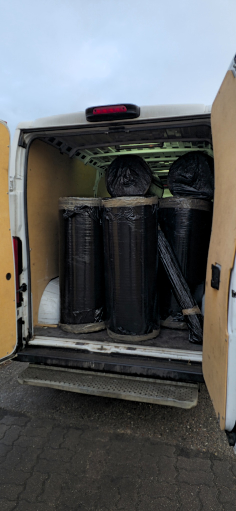 Wnętrze busa z trzema cylindrycznymi ładunkami owiniętymi czarną folią, zabezpieczonymi taśmą. Dodatkowo w tle widoczne worki z ładunkiem.