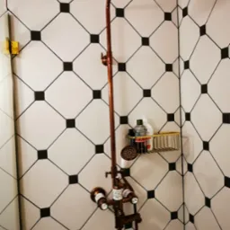 Miedziana armatura prysznicowa na tle białych płytek z czarnymi kwadratami w wykończonej łazience w Akacyjkach. Nowoczesny design.