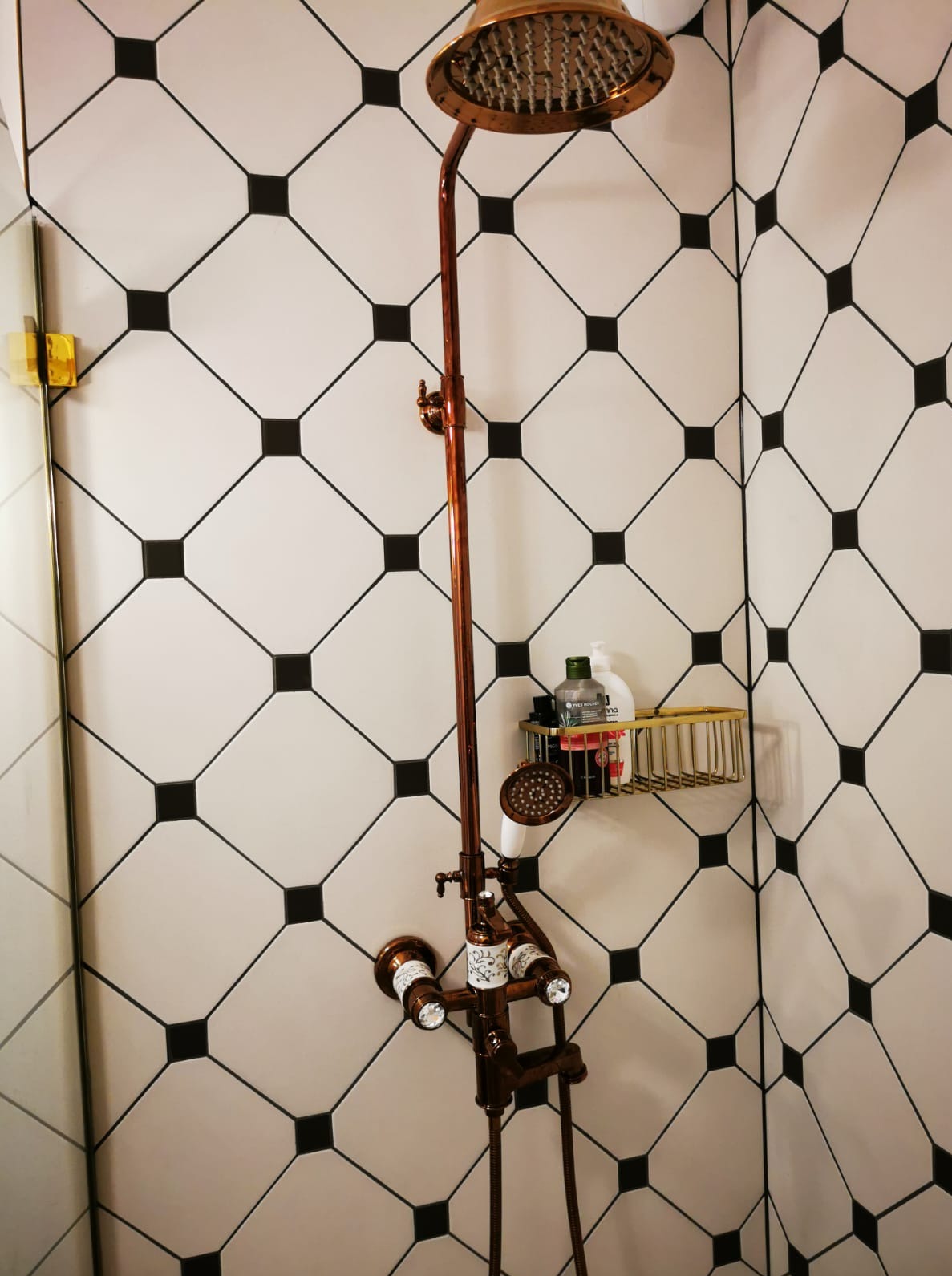 Miedziana armatura prysznicowa na tle białych płytek z czarnymi kwadratami w wykończonej łazience w Akacyjkach. Nowoczesny design.