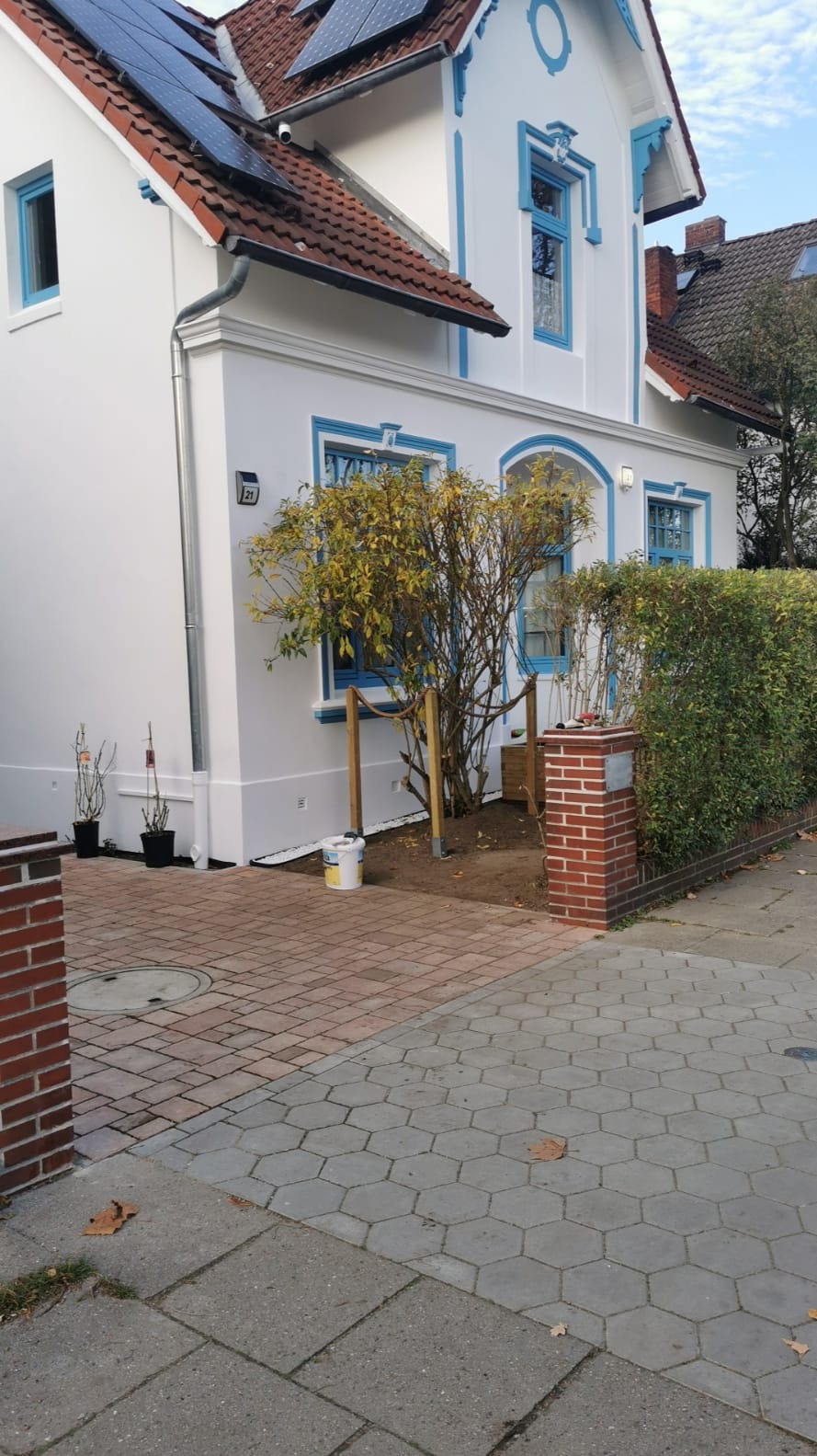 Biały dom z niebieskimi akcentami po renowacji, widoczny z zewnątrz, z odświeżoną elewacją i nowymi panelami słonecznymi na dachu. Na pierwszym planie wiadro z farbą.