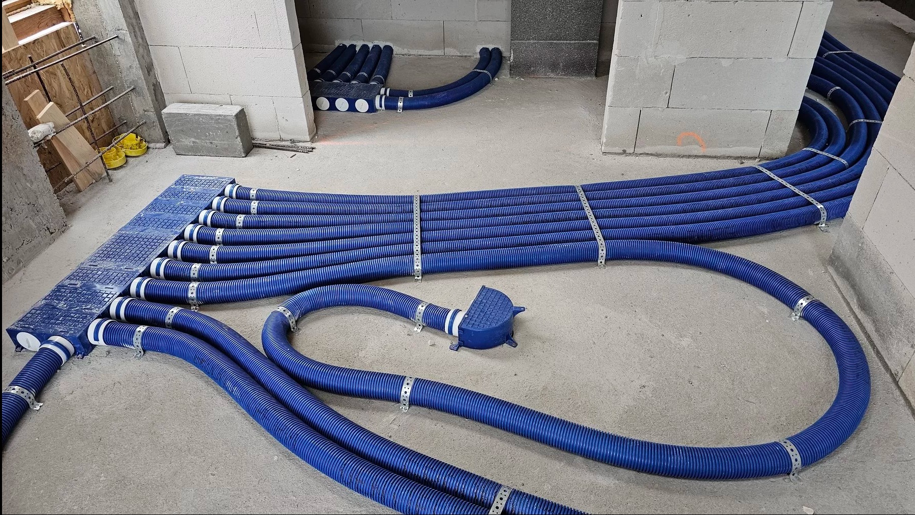 Niebieskie rury wentylacyjne ułożone na podłodze w surowym wnętrzu, z widocznymi elementami montażowymi i fragmentami konstrukcji budynku w tle.