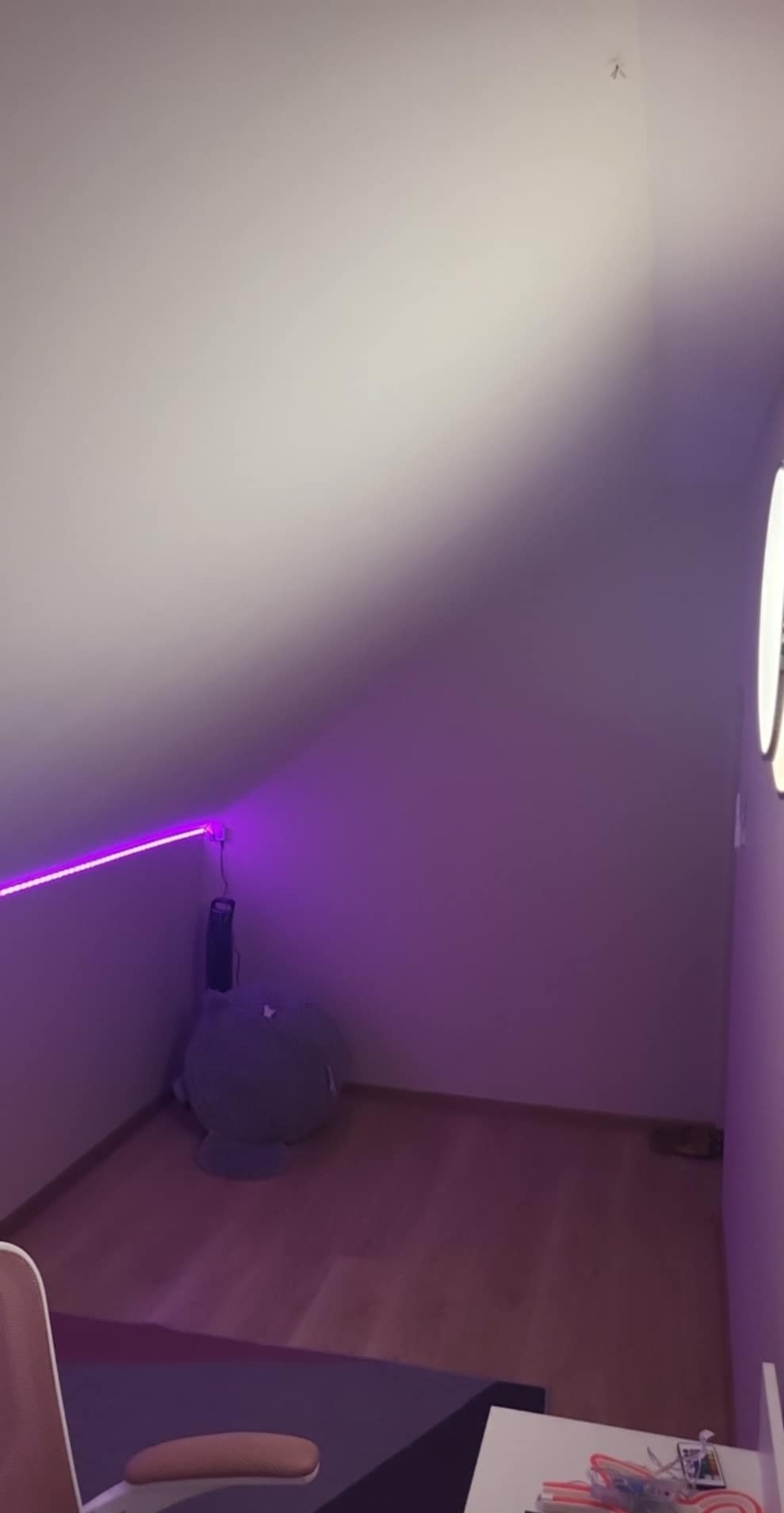 Pokój na poddaszu z fioletowym oświetleniem LED, drewnianą podłogą i ścianami w jasnym odcieniu. Widoczny fragment biurka i krzesła oraz pluszowa zabawka w rogu.